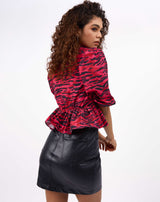 the model looks over her shoulder in the ava puff sleeve pink animal print top showing the peplum over a PU mini skirt
