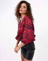 the model is moving her hands while wearing the ava puff sleeve pink animal top with a PU skirt in front of a white background