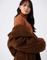 model looks over her shoulder with the gigi brown longline teddy coat shrugged down her shoulders wearing a rust coloured turtleneck