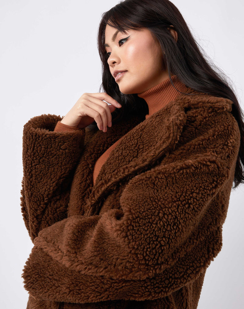 Model looks away from camera with her arm by her face in a cropped image of gigi brown longline teddy coat