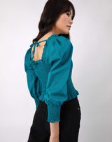 model faces away from the camera wearing the Mia Shirred Green Blouse with tie back with black jeans