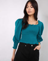 model has her hand in the pocket of her black jeans with the Mia Shirred Green Blouse
