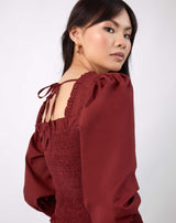 model looks over her shoulder showing the back tie of the mia burgundy shirred blouse