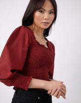 model stands with hands in front of her while wearing the mia burgundy shirred blouse