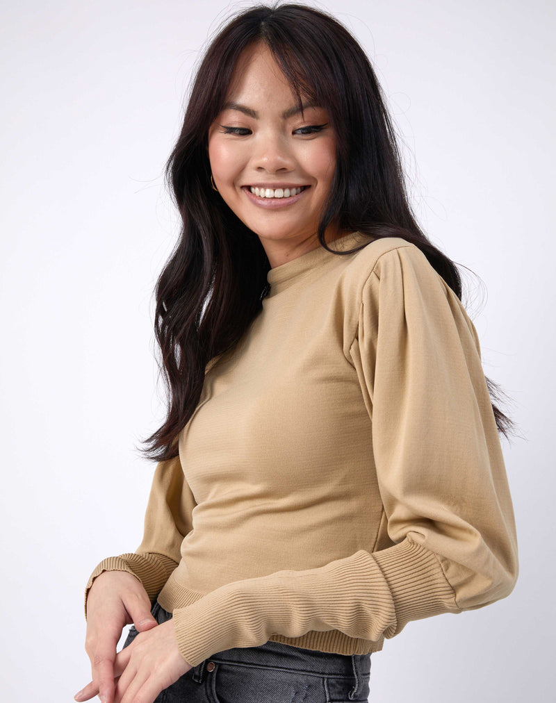 model smiles with her arms in front in a cropped image wearing the nina balloon sleeve knit top in beige