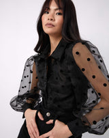 model poses with hands in the pockets of her black jeans while wearing the fifi sheer polka dot blouse with collar and long sleeves