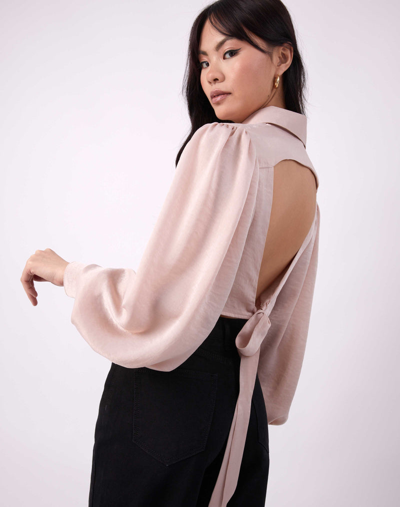 the model faces away from the camera to show the open back of the fifi satin shirt in champagne with a tie back alongside black jeans