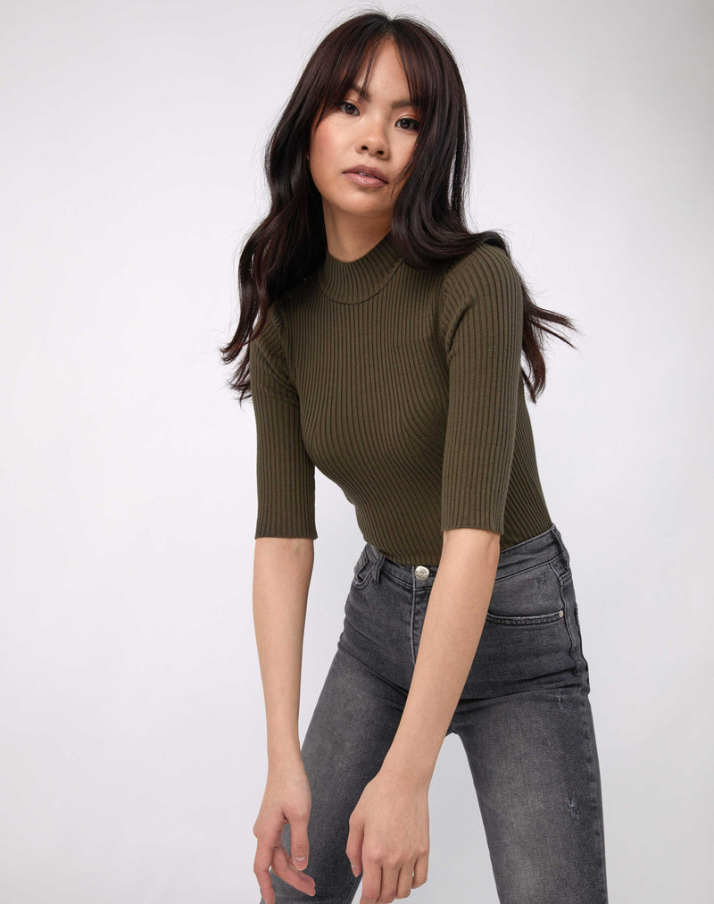 model leans towards camera in the olive meg ribbed mid sleeve bodysuit in black with grey jeans