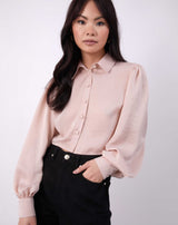 the model poses with her hand in her pocket of her black jeans wearing the fifi satin open back shirt with button up front