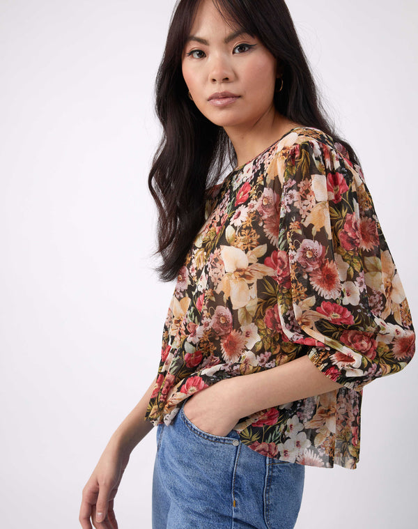 a cropped image of the model with her hand in the pocket of her blue jeans wearing the floral floral sheer puff sleeve top