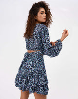 model faces away from the camera and holds her arm wearing the Maeve Tie Back Floral Top and matching skirt