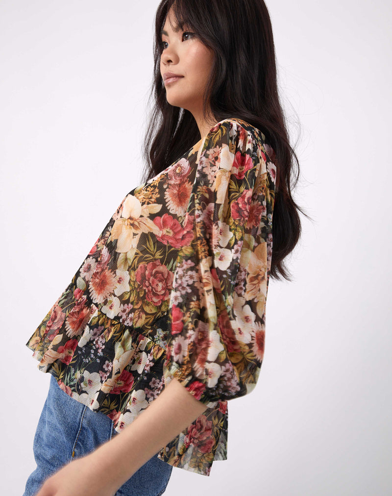 a cropped image of the model from the side in the flora floral sheer puff sleeve top with blue jeans