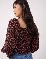 model looks over her shoulder wearing the adele shirred blouse  in pink rose print with jeans in front of a white background