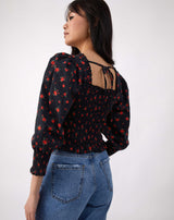 model looks away from camera wearing the mia red rose print shirred blouse with blue jeans, showing the tie back