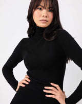 close up image of model with hands on her hips the liana black roll neck knit midi dress 