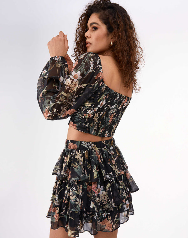 model faces away from the camera wearing the Marina Black Floral Gathered Top with matching tiered skirt