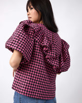 model shows the back of the laila pink and black check frill top with puff sleeves worn with blue jeans