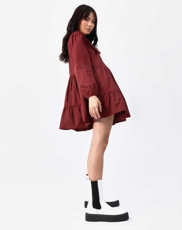 model standing sideways in red alice collared cotton dress in white boots against white background