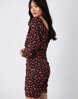 the model wears the annie gathered dress in pink florals while looking over her shoulder in front of a white background