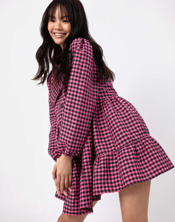 model moves wearing pink and black check alice collared dress while smiling against white background