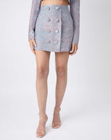 a cropped image of the model in the claudia iridescent skirt in pink and blue with buttons down the front with nude heels