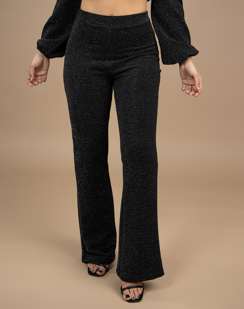 model wears wide leg lurex trousers in black with heels and her hands by her side in a cropped image in front of a beige background