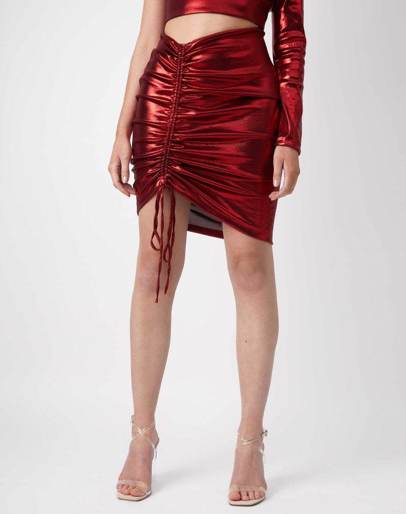 cropped close image of model wearing the kourt red ruched shiny skirt with nude perspex heels