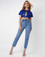 a full image shot of the model wearing the Miley Blue Shimmer Tie Crop Top with blue jeans and perspex heels