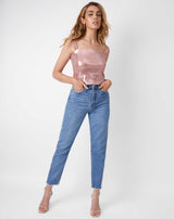 a full length picture of the model wearing the chi sparkly pink corset top with her hands in the pockets of her blue jeans with nude heels