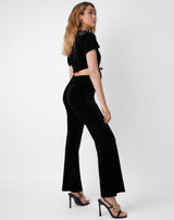model looks over her shoulder while wearing brudget black velvet wide leg trousers from the back with matching top and black heels