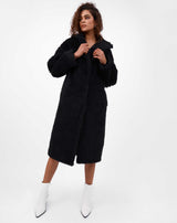 model holds jacket lapel of gigi black teddy longline coat with white boots