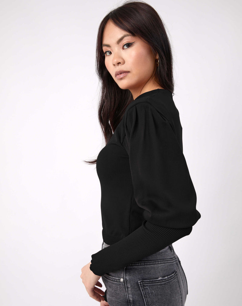 model looks towards the camera in the nina balloon sleeve knit top in black with grey jeans