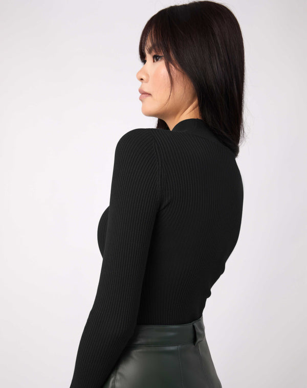 we see the back of the model wearing the lorna black turtleneck ribbed knit bodysuit with green pu skirt