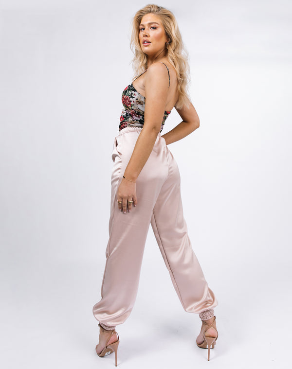 model looks over her shoulder showing the back of the kyla champagne satin joggers with the floral mesh bodysuit