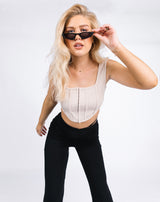 Model leans towards the camera holding her sunglasses while wearing the Lauren Corset Top in Oyster Rib with black trousers