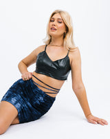 the model sits on the floor wearing the Remi Blue Tie Dye Ruched Skirt with a pu crop top