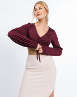 the model is holding her hands in front of her while wearing the Skye Ruched Front Crop Top in Grape with nude ribbed skirt
