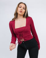 the model holds the tie of the Frankie Ribbed Tie Front Top & Bandeau in Raspberry worn with black skinny jeans