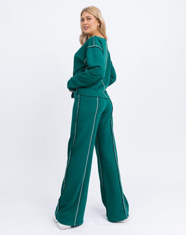 a full length image of the model from behind wearing the Chantelle Contrast Stitch Logo Trousers in Forest Green with matching naz top