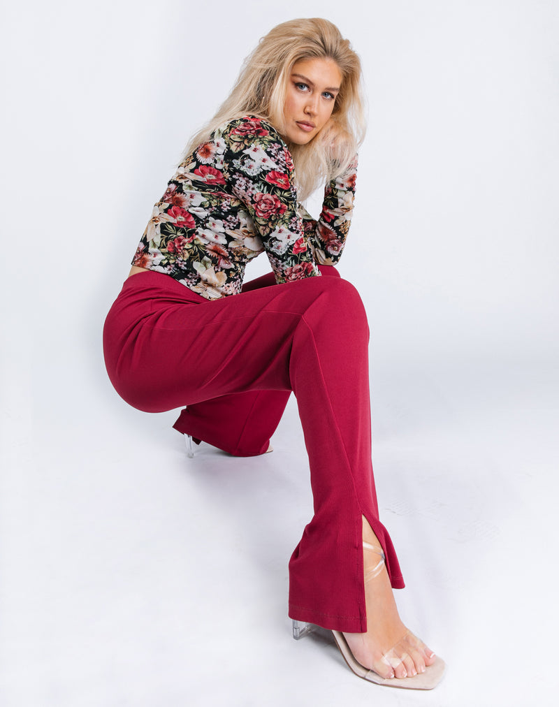 the model crouches wearing Lana Wide Leg Trousers in Raspberry Rib with heels and floral top