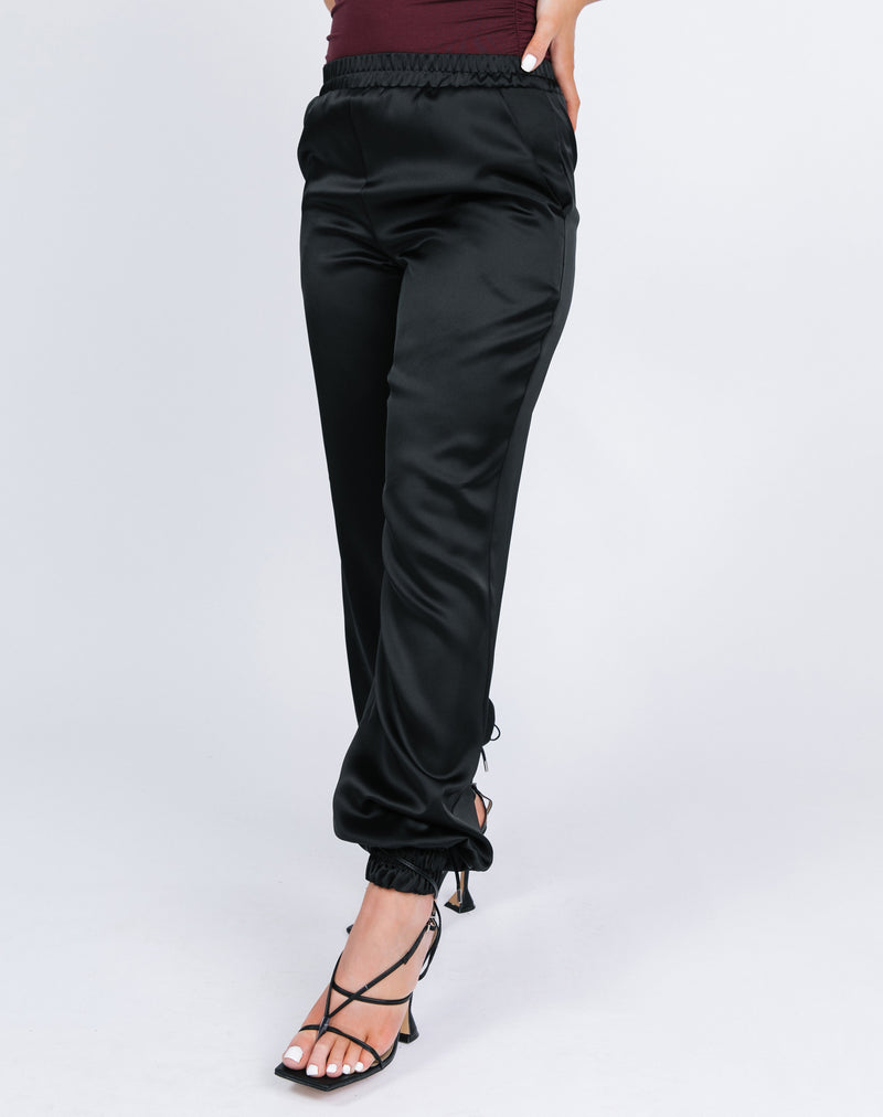 a cropped close up shot of model wears the kyla black satin joggers with a red bodysuit and black tie up heels