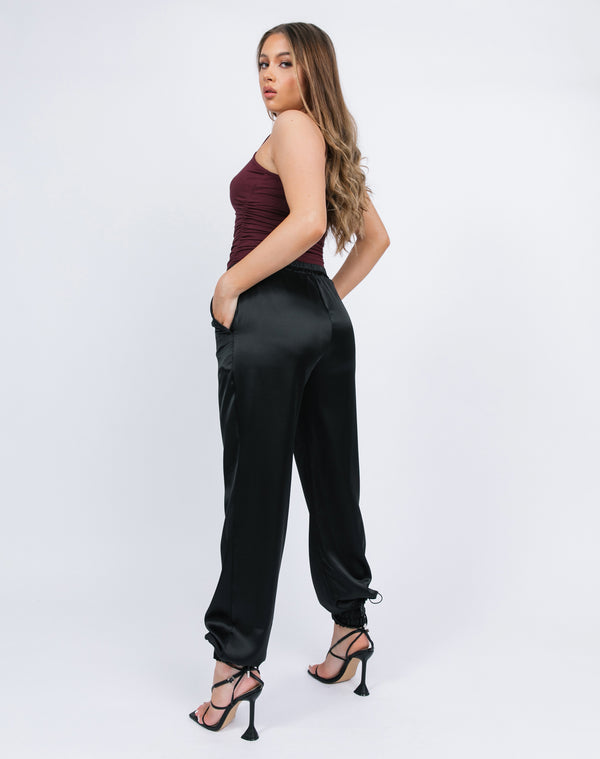 model wears the kyla black satin joggers with a red bodysuit and black tie up heels showing us the back
