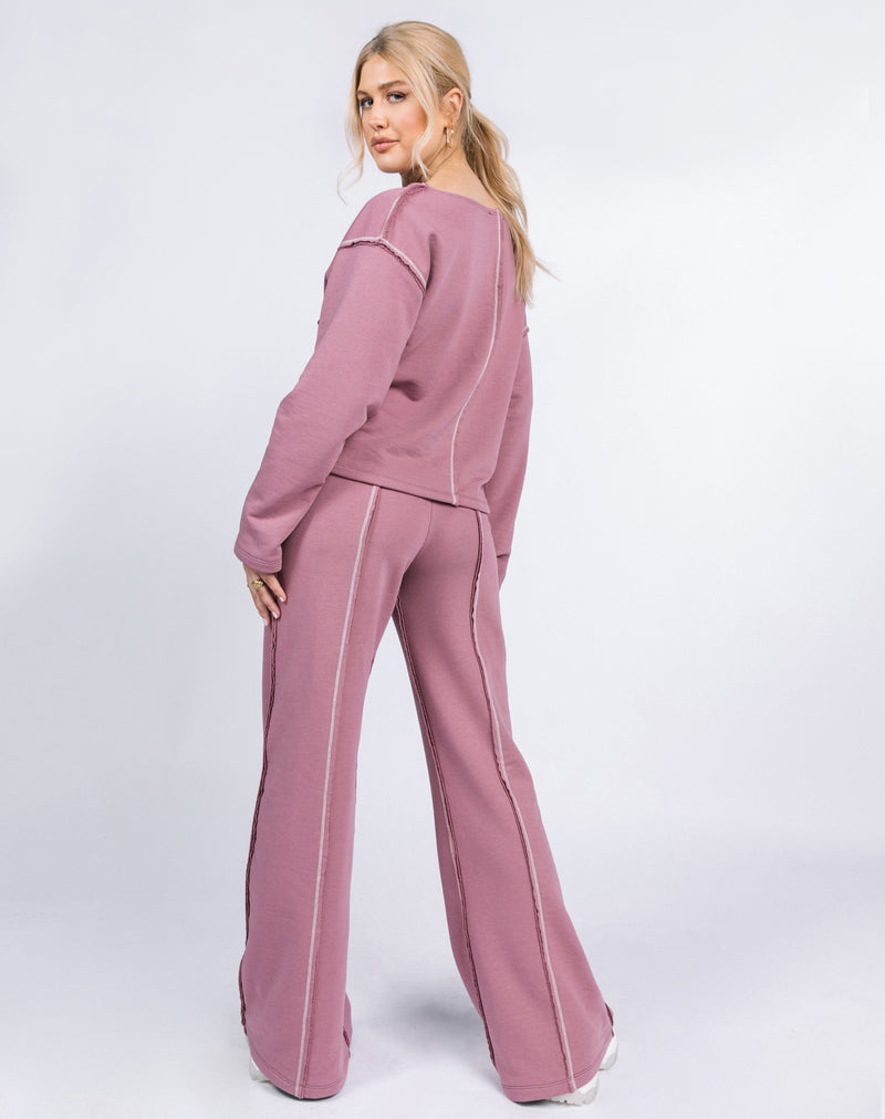 the model looks over her shoulder to show the back of the Naz Contrast Stitch Logo Jumper in Blush worn with the matching trousers