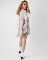 the model looks over her shoulder wearing Regina Satin Babydoll Dress in Silver and white boots