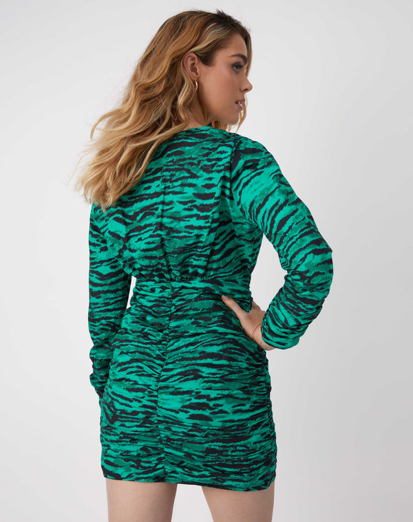 a model looks over her shoulder while we see the back of the esme green animal print dress with one hand on her him