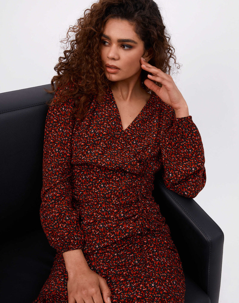 model sits on a black armchair leaning on her arm wearing the Ruby Red Floral Ruched Wrap Dress
