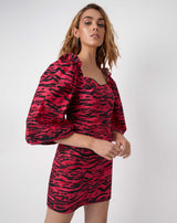 the model looks at the camera with hands in front of her wearing the charlotte pink animal zebra print puff sleeve dress